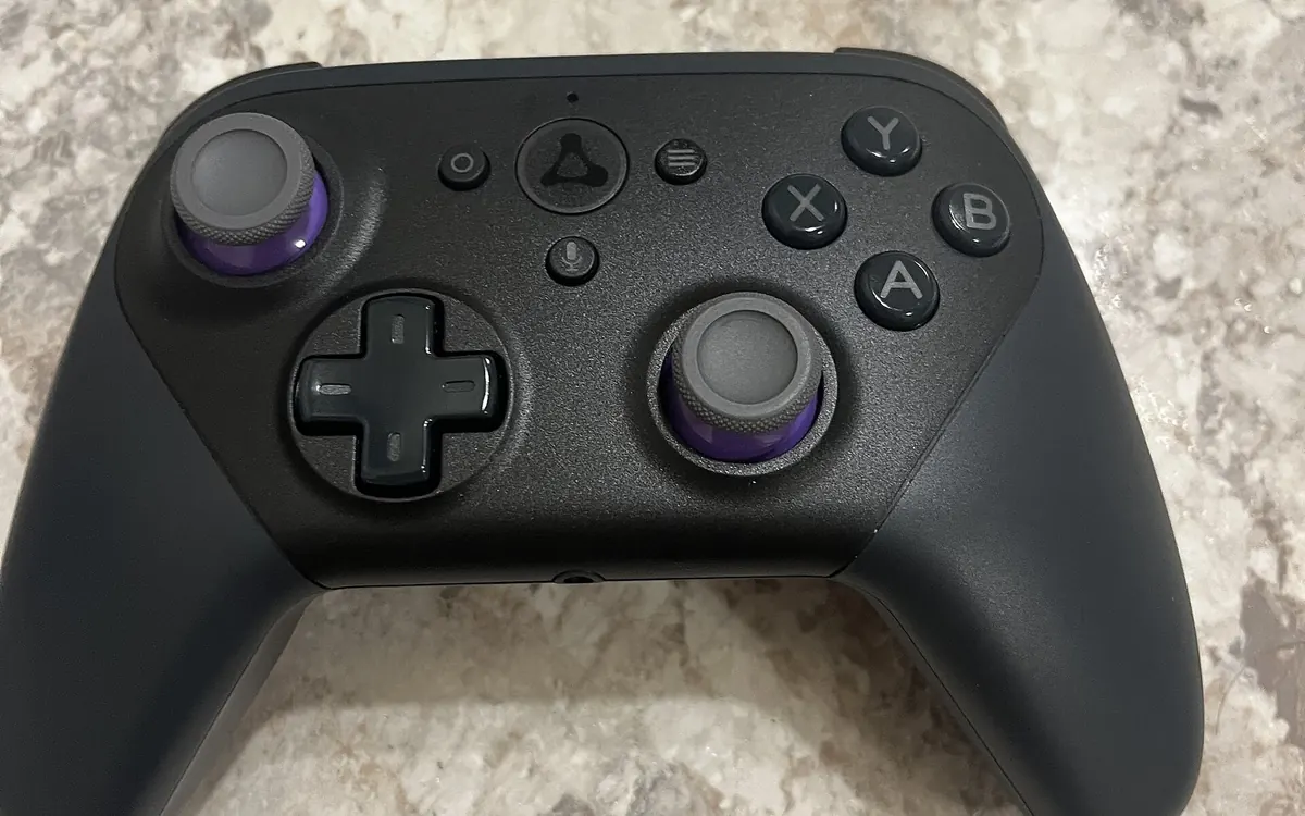 Black Amazon Luna wireless game controller with purple-ringed thumbsticks on a stone countertop