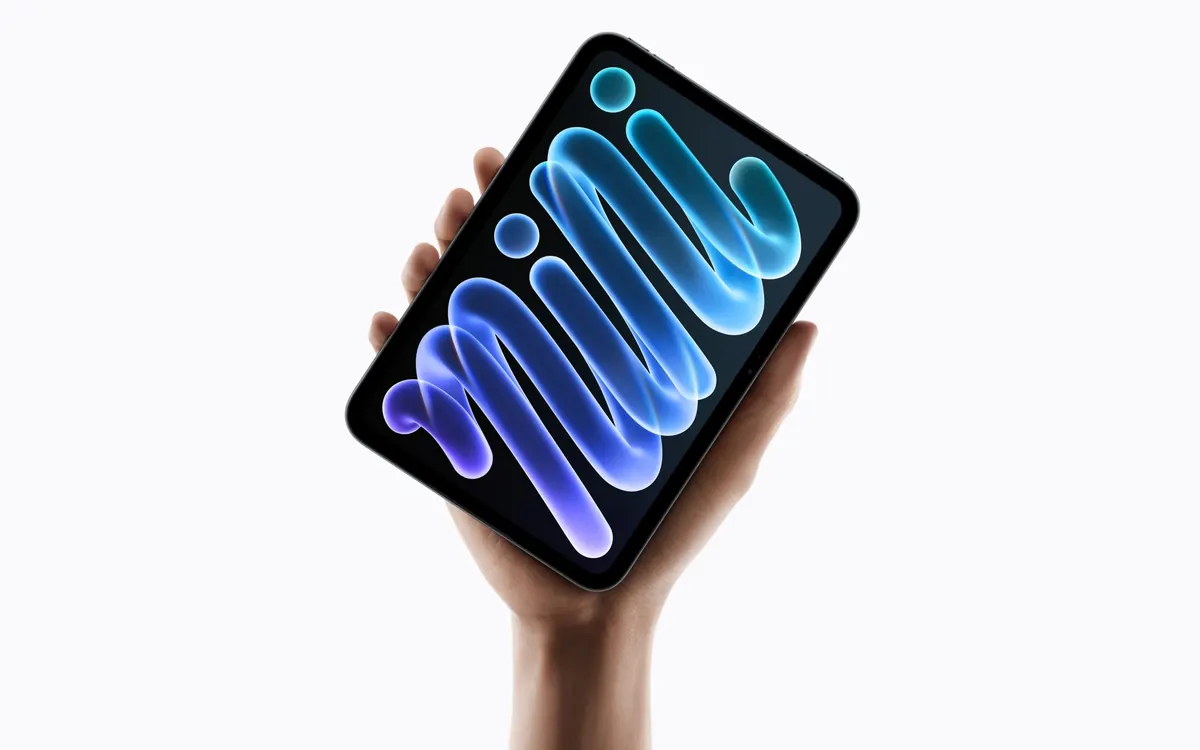 A hand holding the new iPad mini with its OLED display showing a colourful abstract wallpaper