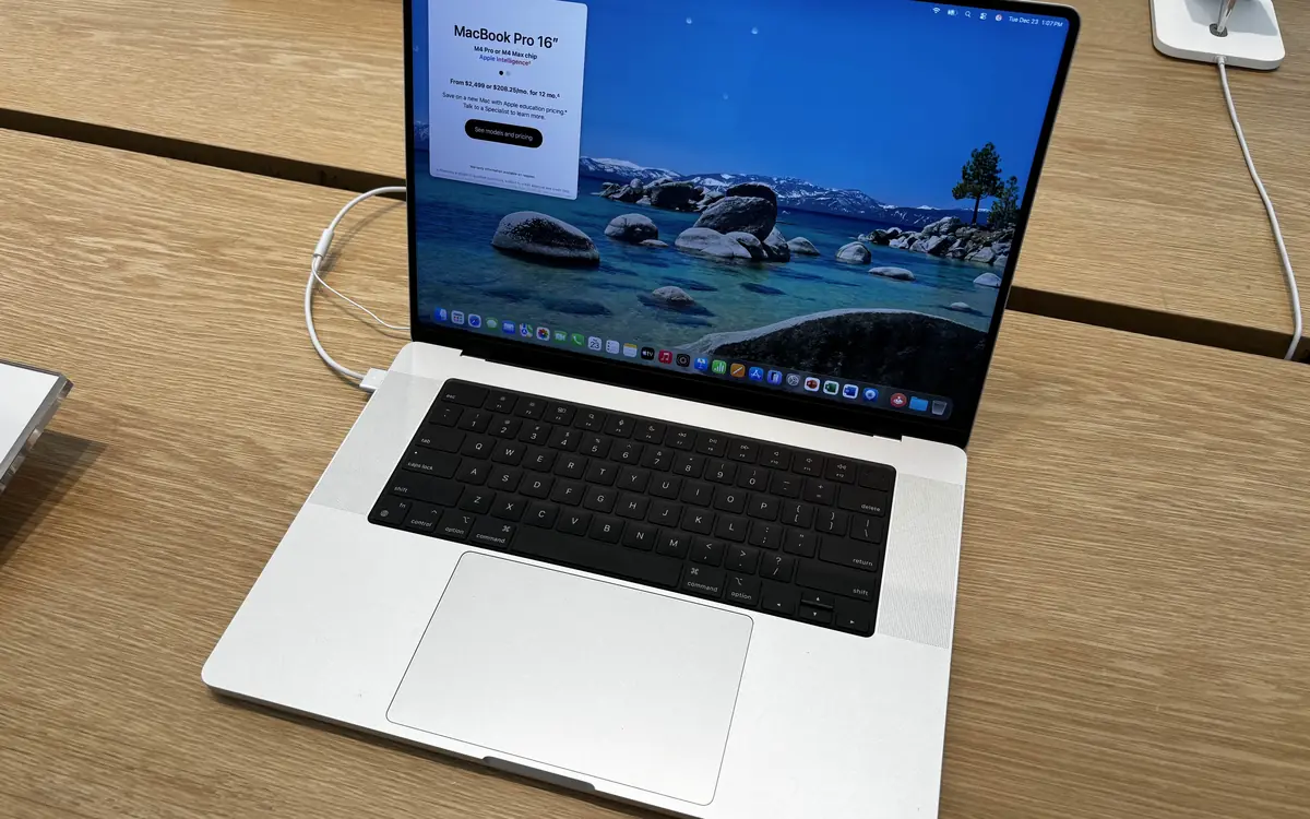 A silver 16-inch MacBook Pro open on a wooden table in a store (illustrative photo)