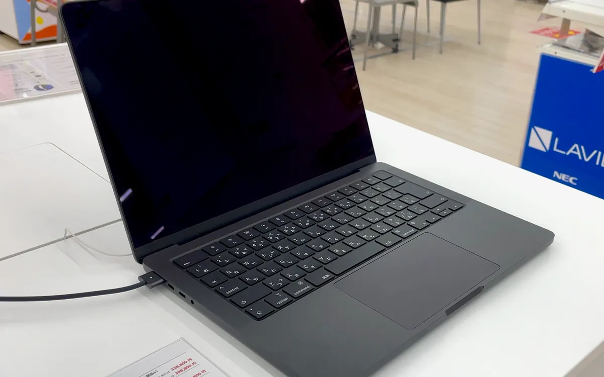 An open 14-inch MacBook Pro in Space Grey on a white display table in a Japanese electronics store (illustrative photo of a current non-touch model)