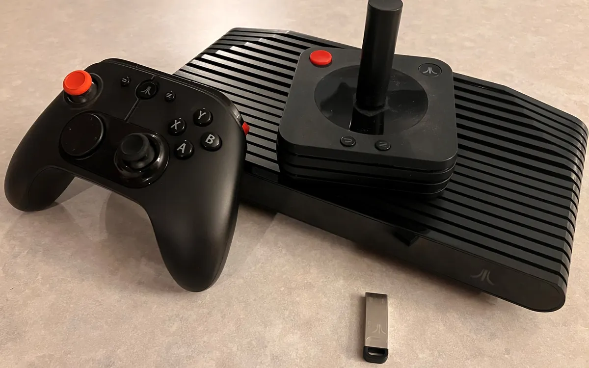 Black Atari VCS console with its modern gamepad and classic-style joystick on a table