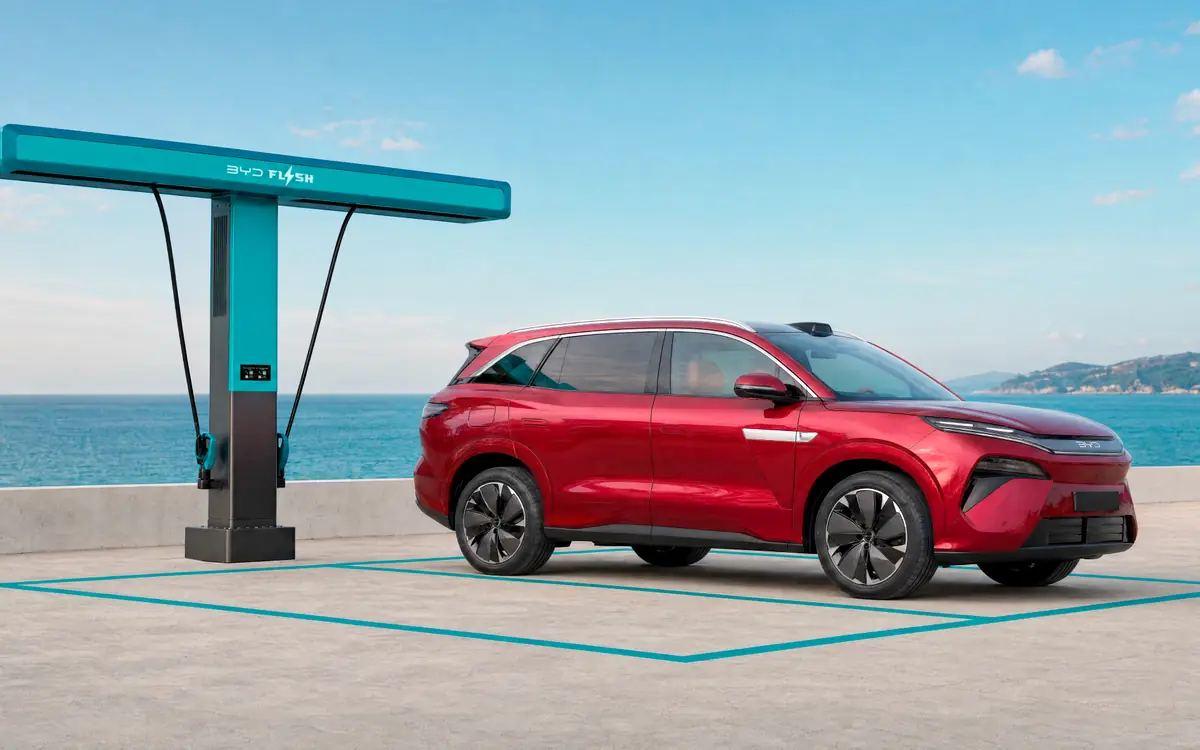 A red BYD Atto 8 electric SUV parked at a BYD Flash Charging station by the sea