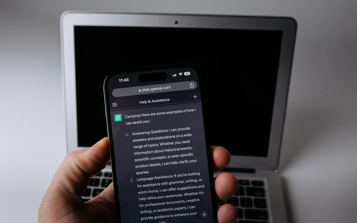 A smartphone showing the ChatGPT app held in front of an open laptop (illustrative photo)
