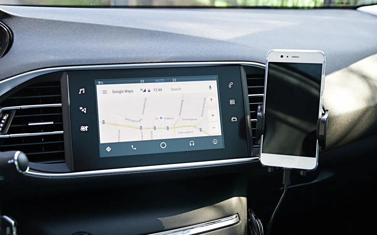 Android Auto running on a car's dashboard screen with a smartphone mounted beside it (illustrative photo, older Android Auto interface)