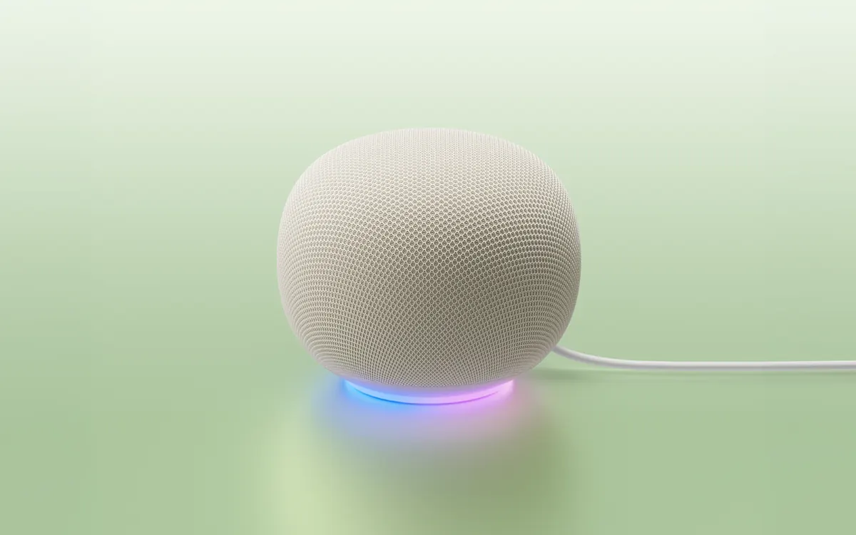Official product image of the white Google Home Speaker, a round fabric-covered speaker with a coloured light ring at its base