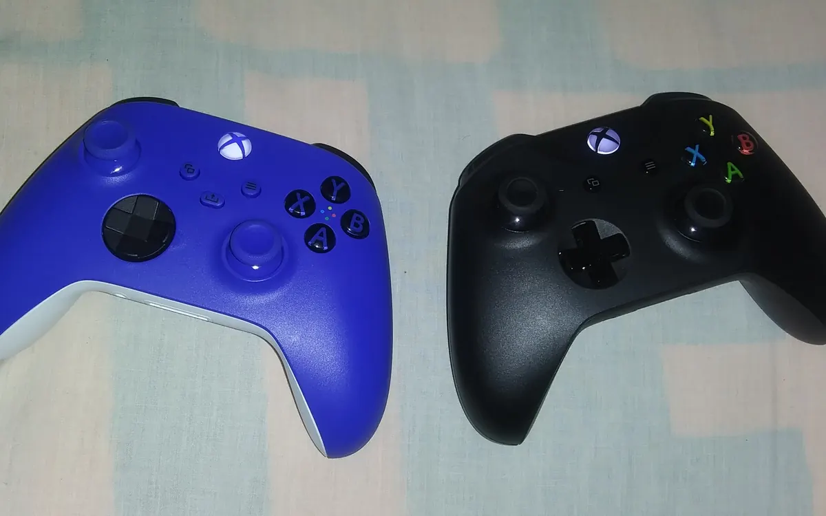 Синій бездротовий контролер Xbox Series X|S поруч із чорним контролером Xbox One на покривалі (ілюстративне фото)