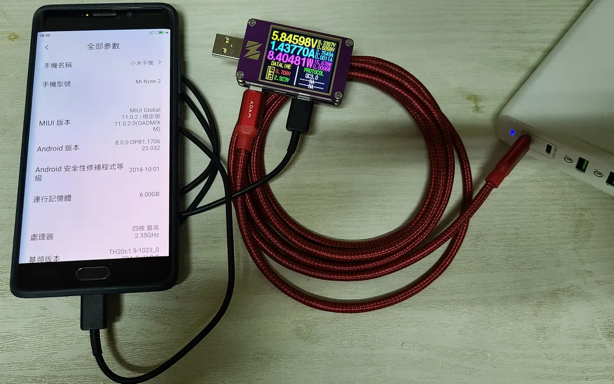 Смартфон заряжается через плетёный USB-кабель со встроенным USB-тестером, показывающим напряжение и ток