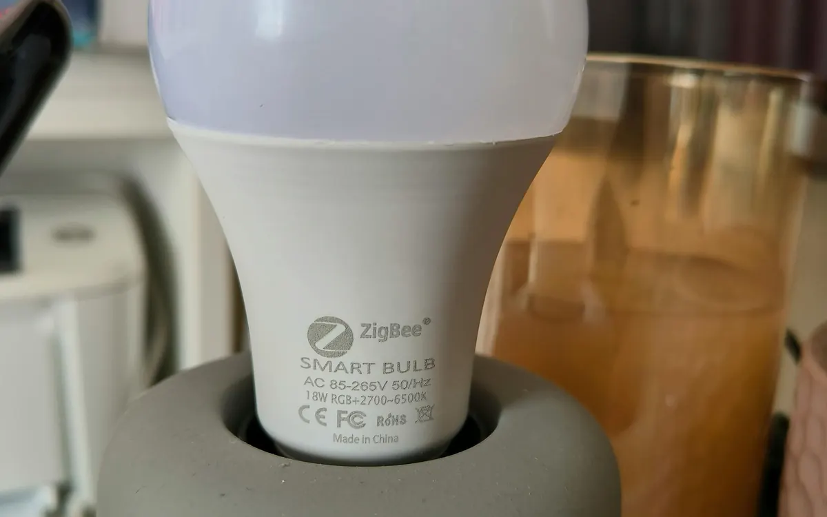 A Zigbee smart bulb with an E27 base held in a hand (illustrative photo)