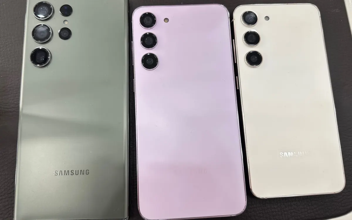 The backs of a green Galaxy S23 Ultra, a lavender Galaxy S23+ and a cream Galaxy S23 side by side on a dark table