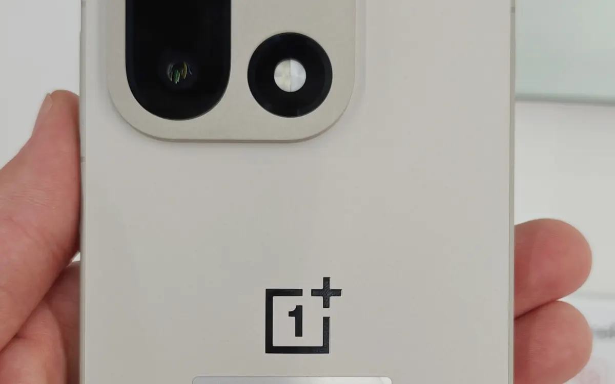 The back of a white OnePlus 15 held in a hand
