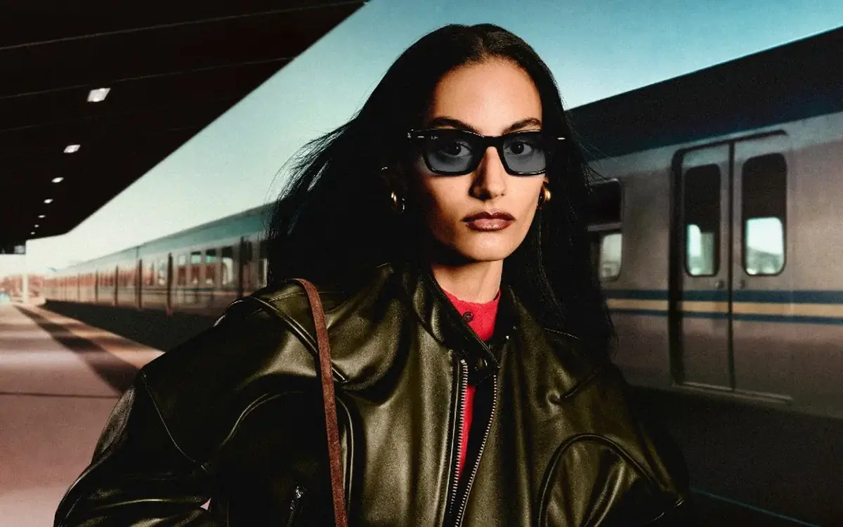 A woman wearing black Ray-Ban Meta Audio glasses in the Burbank style on a train platform (Meta promotional image)