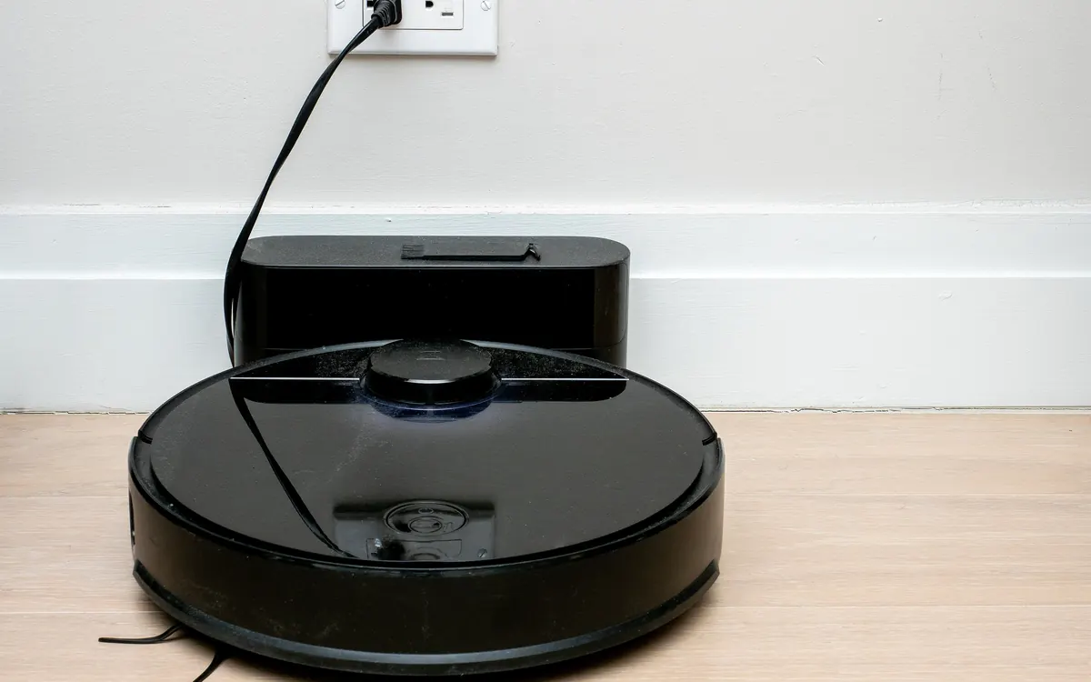 A black Roborock robot vacuum charging on its dock against a white wall (illustrative photo)