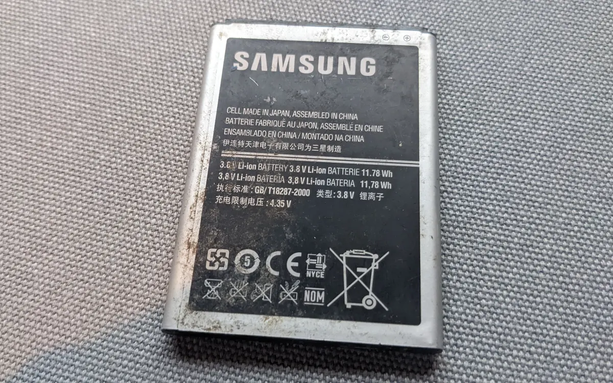 A Samsung lithium-ion smartphone battery lying on a grey surface (illustrative photo)