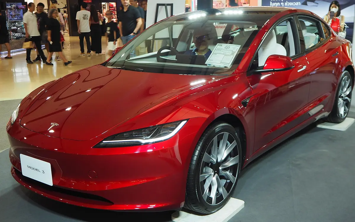 A red Tesla Model 3 (Highland) on display at an indoor car show (illustrative photo)