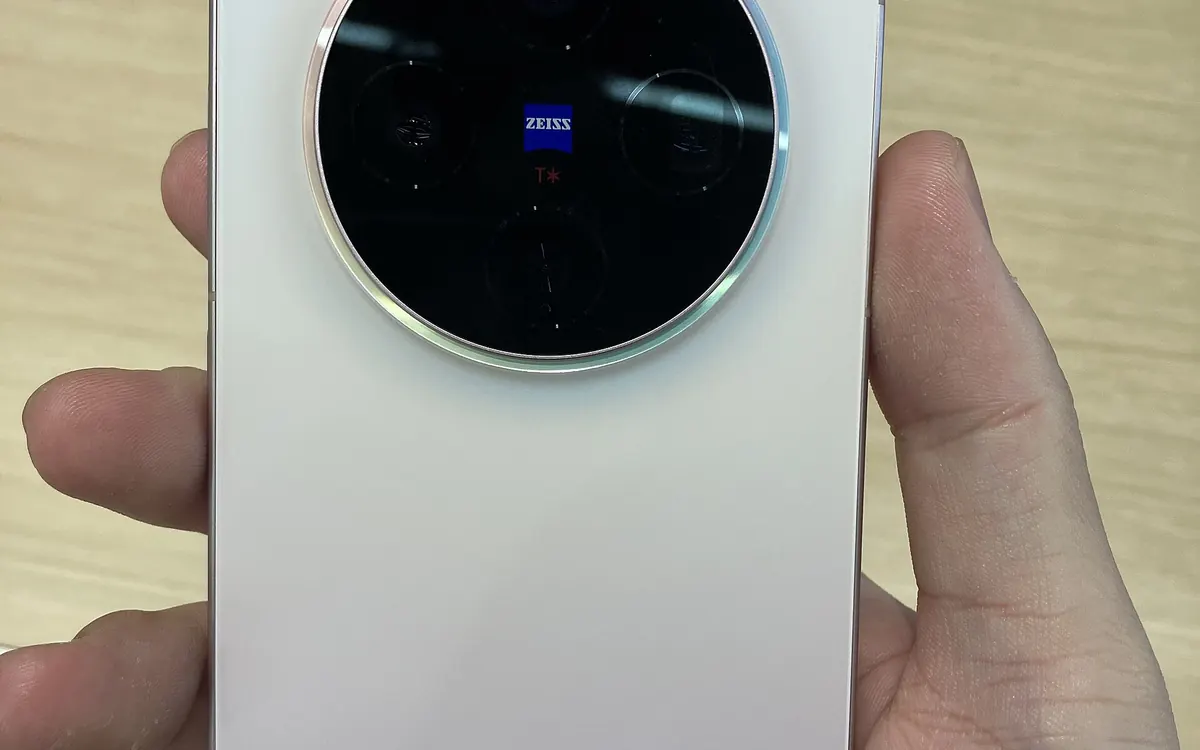 Back of a white vivo X300 smartphone held in a hand, a different vivo model (illustrative photo)