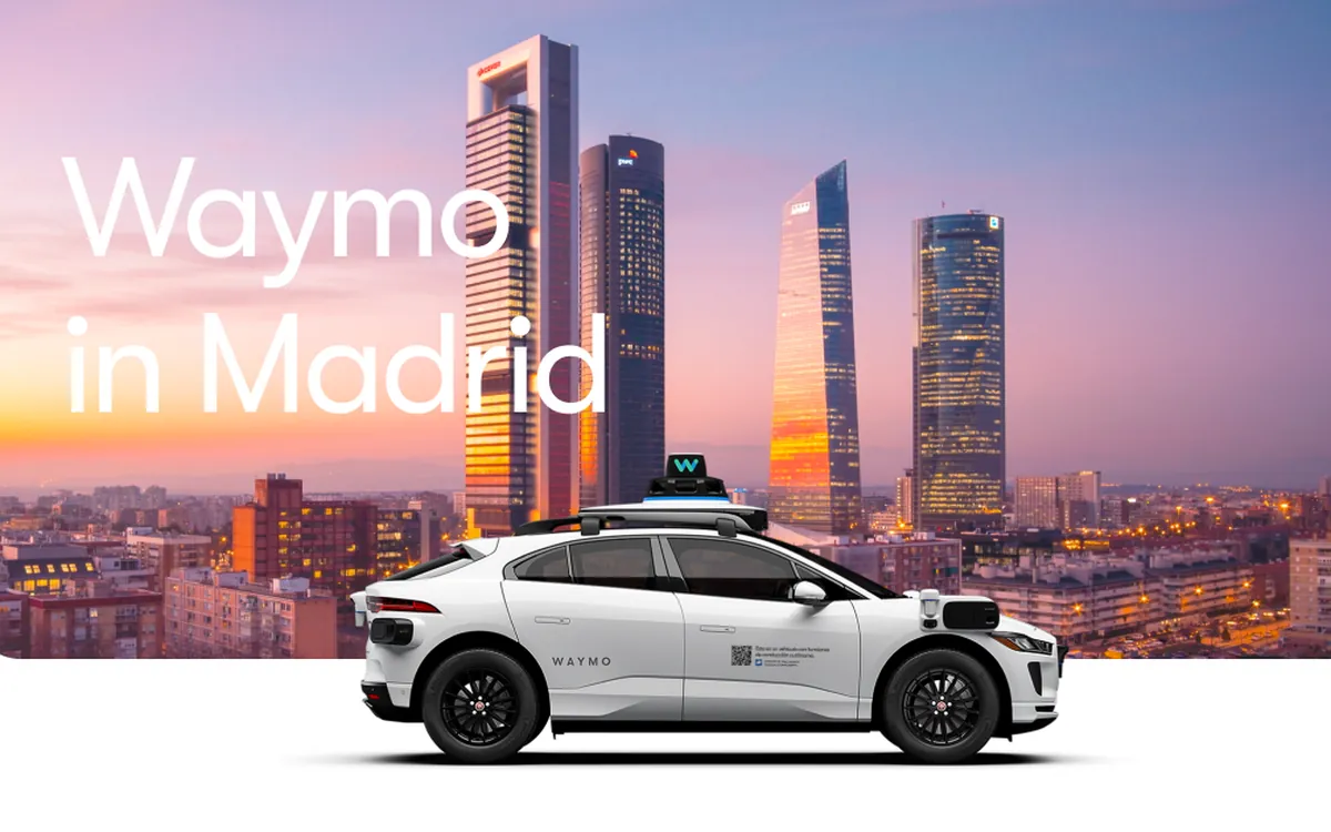 Рекламне зображення Waymo: біле роботаксі Jaguar I-PACE на тлі хмарочосів Мадрида на заході сонця з написом Waymo in Madrid